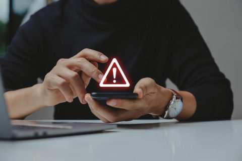 A person holding a smartphone displaying a glowing red warning triangle symbol