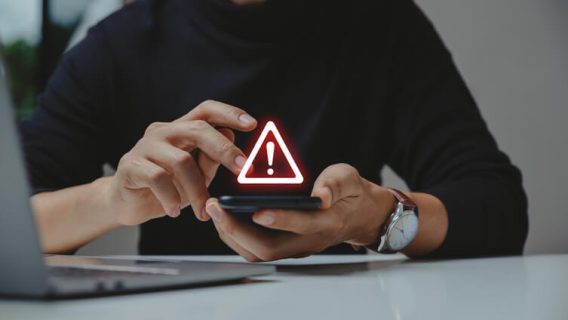 A person holding a smartphone displaying a glowing red warning triangle symbol