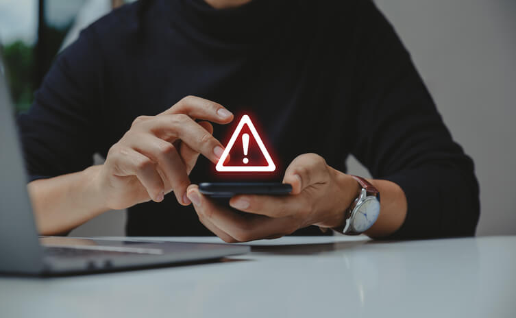 A person holding a smartphone displaying a glowing red warning triangle symbol