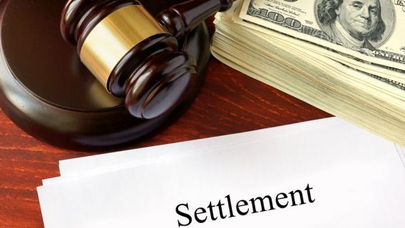 gavel with a stack of hundred dollar bills over a settlement form